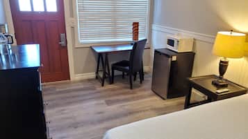 A hotel room with a bed, a desk with a chair, a refrigerator, a microwave, a lamp, and a window with blinds.