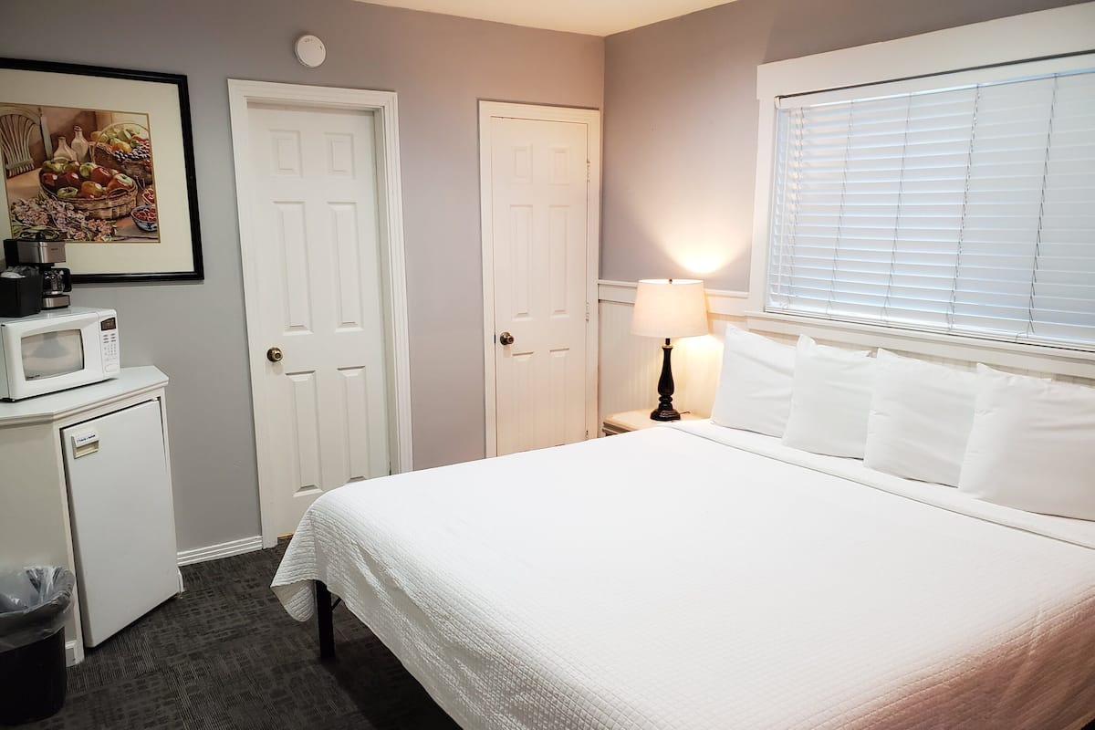 A hotel room with a bed, a nightstand with a lamp, a microwave, and a trash bin.