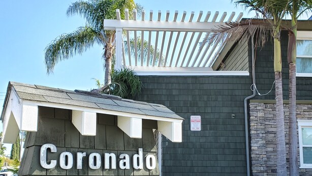 Un senyal de fusta de Coronado Island Inn, amb una pérgola i palmeres al fons.