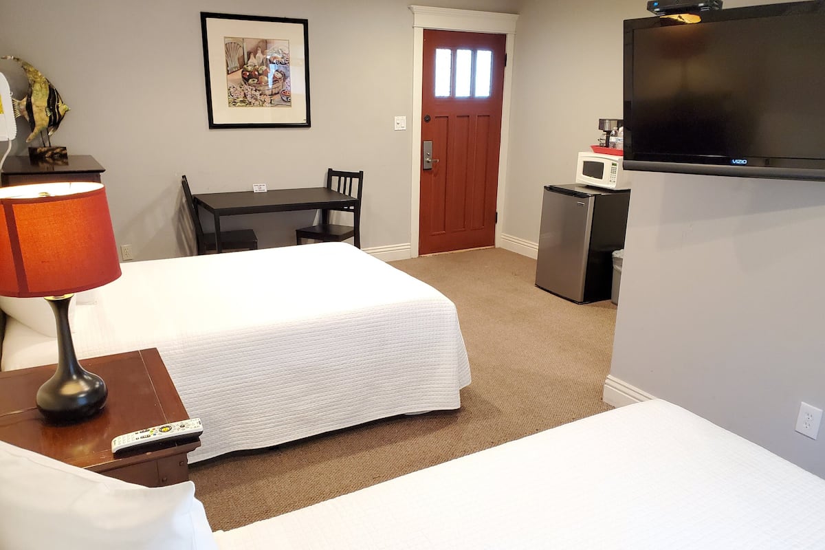 A hotel room with two beds, a desk, a chair, a TV, a microwave, and a refrigerator.