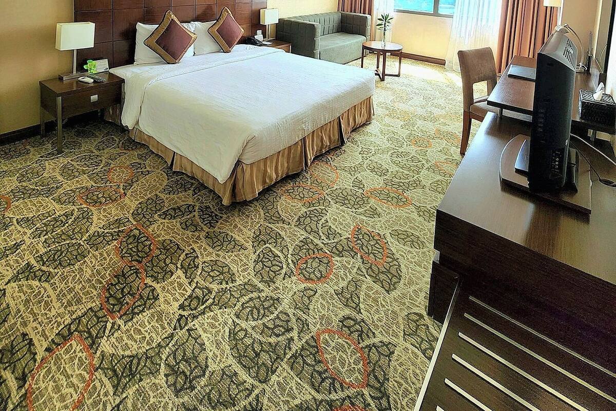 Une chambre d’hôtel avec un grand lit, un bureau avec un ordinateur, une chaise, une petite table et une fenêtre avec des rideaux.
