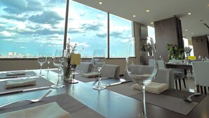 Un comedor moderno con mesas dispuestas para cuatro, ventanas amplias con vistas a la ciudad y un interior luminoso y bien iluminado.