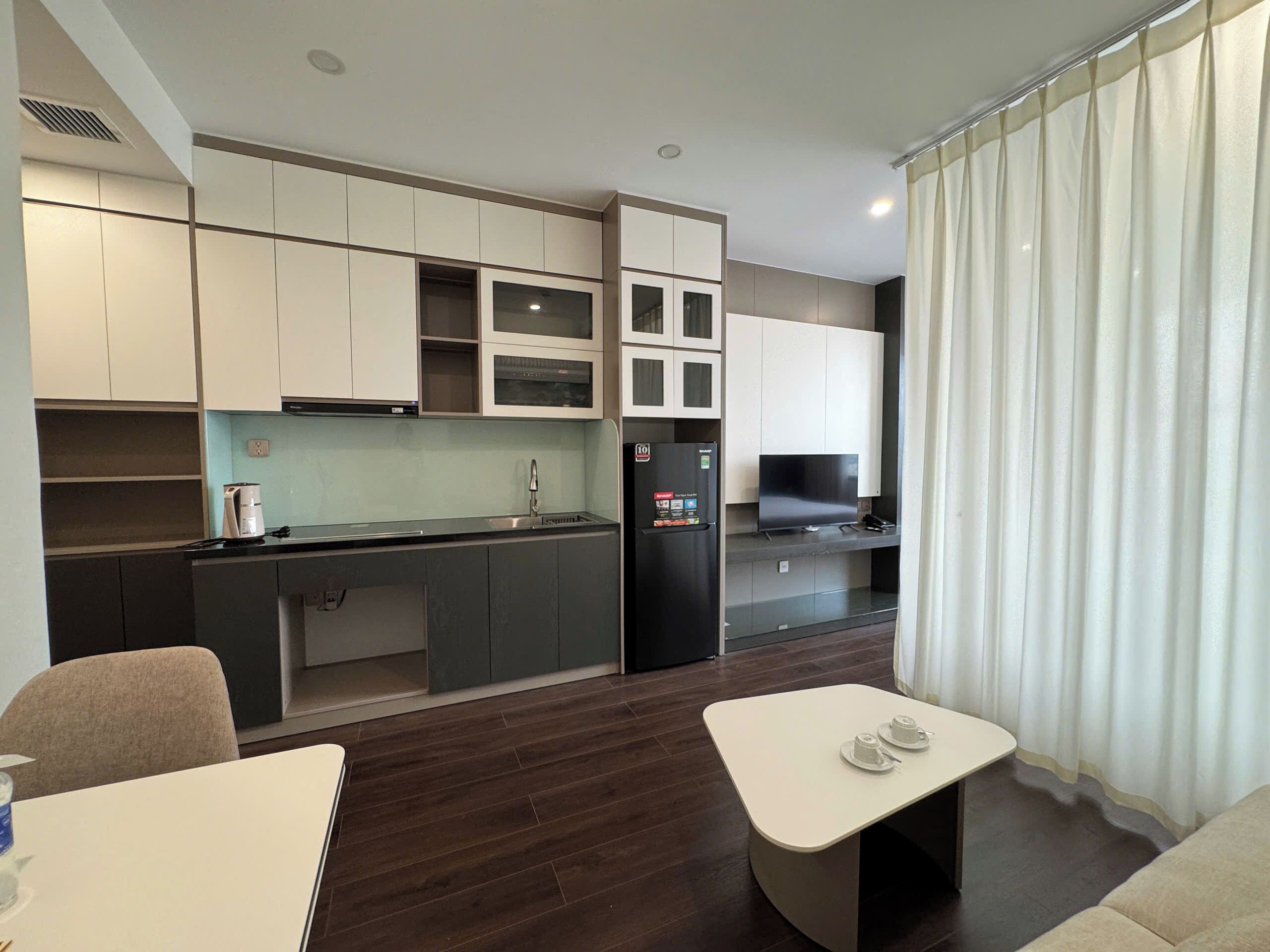 Une cuisine moderne avec un plancher en bois foncé, des meubles blancs et un réfrigérateur noir.