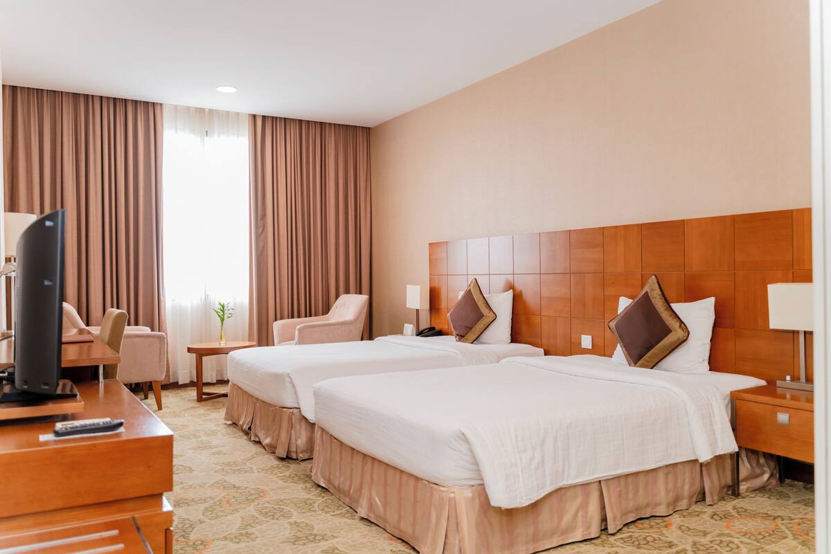 Une chambre d’hôtel avec deux lits, un bureau avec une télévision, une chaise, une petite table et une lampe.