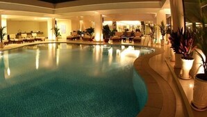 Una piscina interior de diseño curvo, rodeada de zonas de descanso y plantas en macetas.