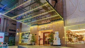 Entrada de un hotel con un letrero que dice "AURORA HOTEL PLAZA" y estatuas decorativas.