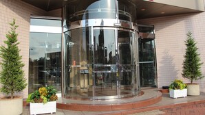 A hotel entrance with a revolving door, glass doors, and potted plants. - Hotel Resol Sasebo (Sasebo)