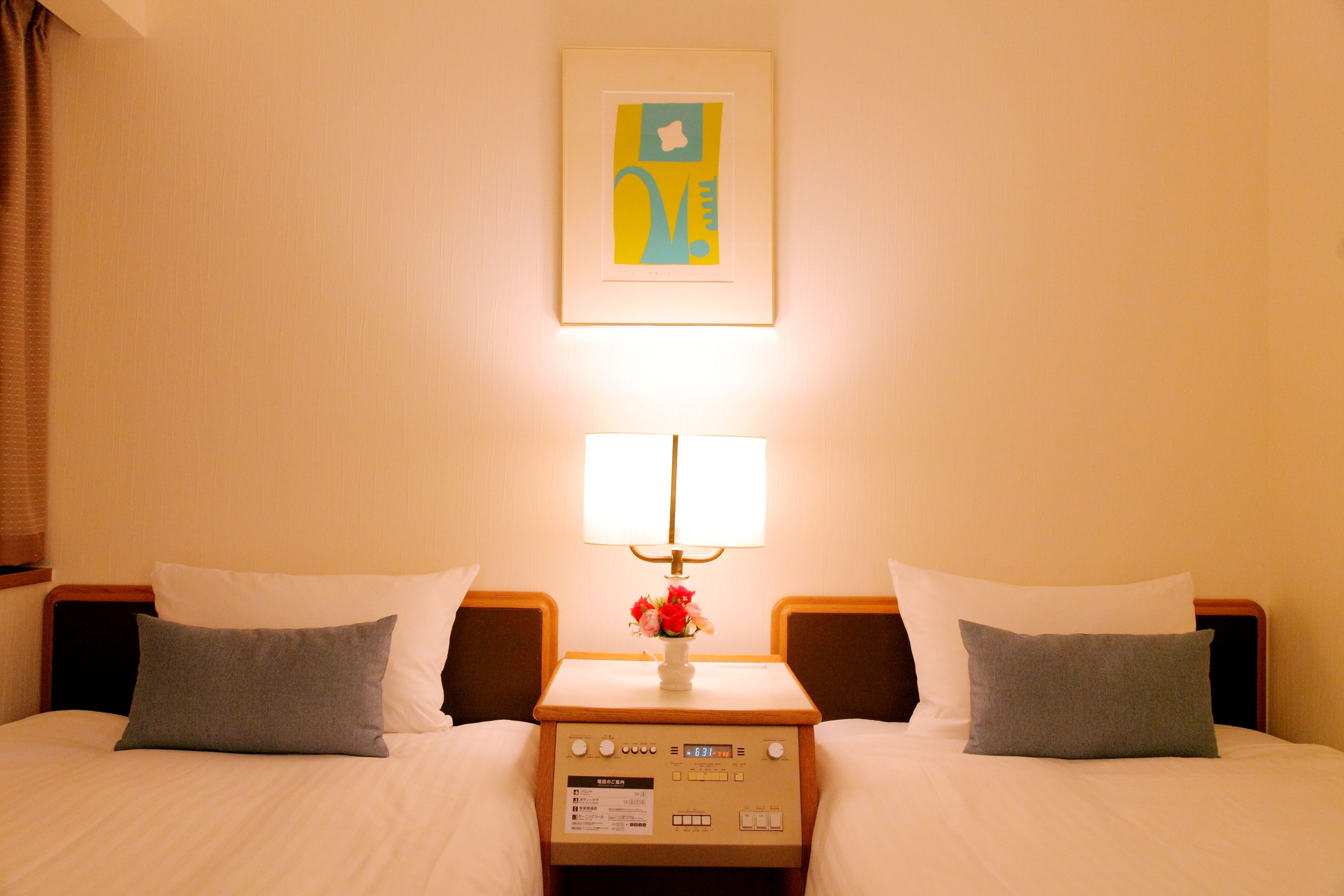 Una habitación de hotel con dos camas, una mesita de noche con lámpara y un cuadro en la pared.