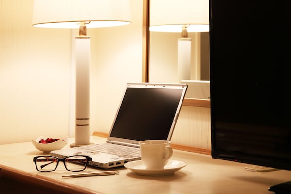 A laptop on a desk with a cup and glasses, a bowl of flowers, and a lamp. - Hotel Resol Sasebo (Sasebo)