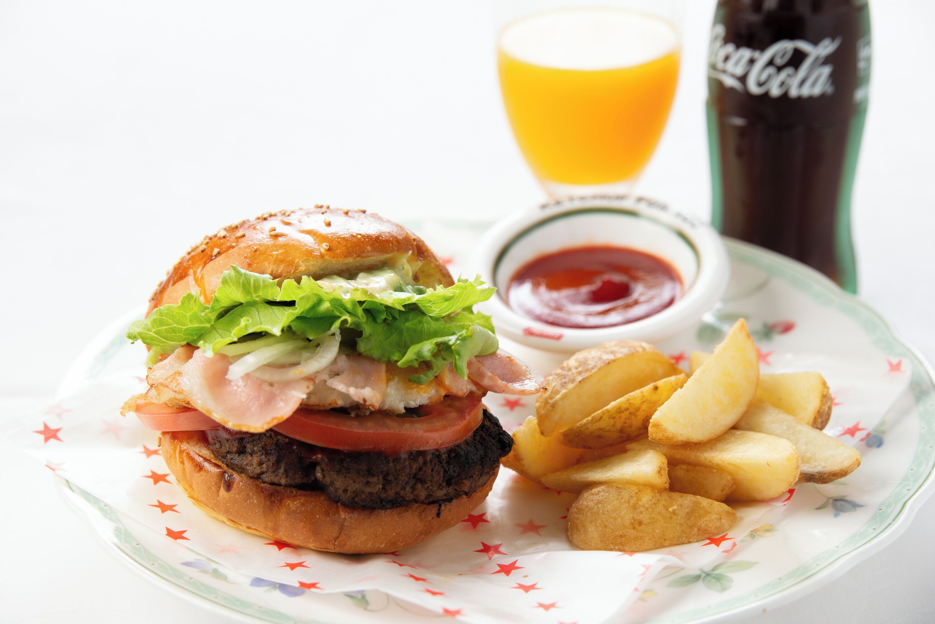 A burger with lettuce, tomato, and bacon, served with fries and ketchup, and a glass of orange juice.