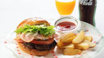 A burger with lettuce, tomato, and bacon, served with fries and ketchup, and a glass of orange juice.