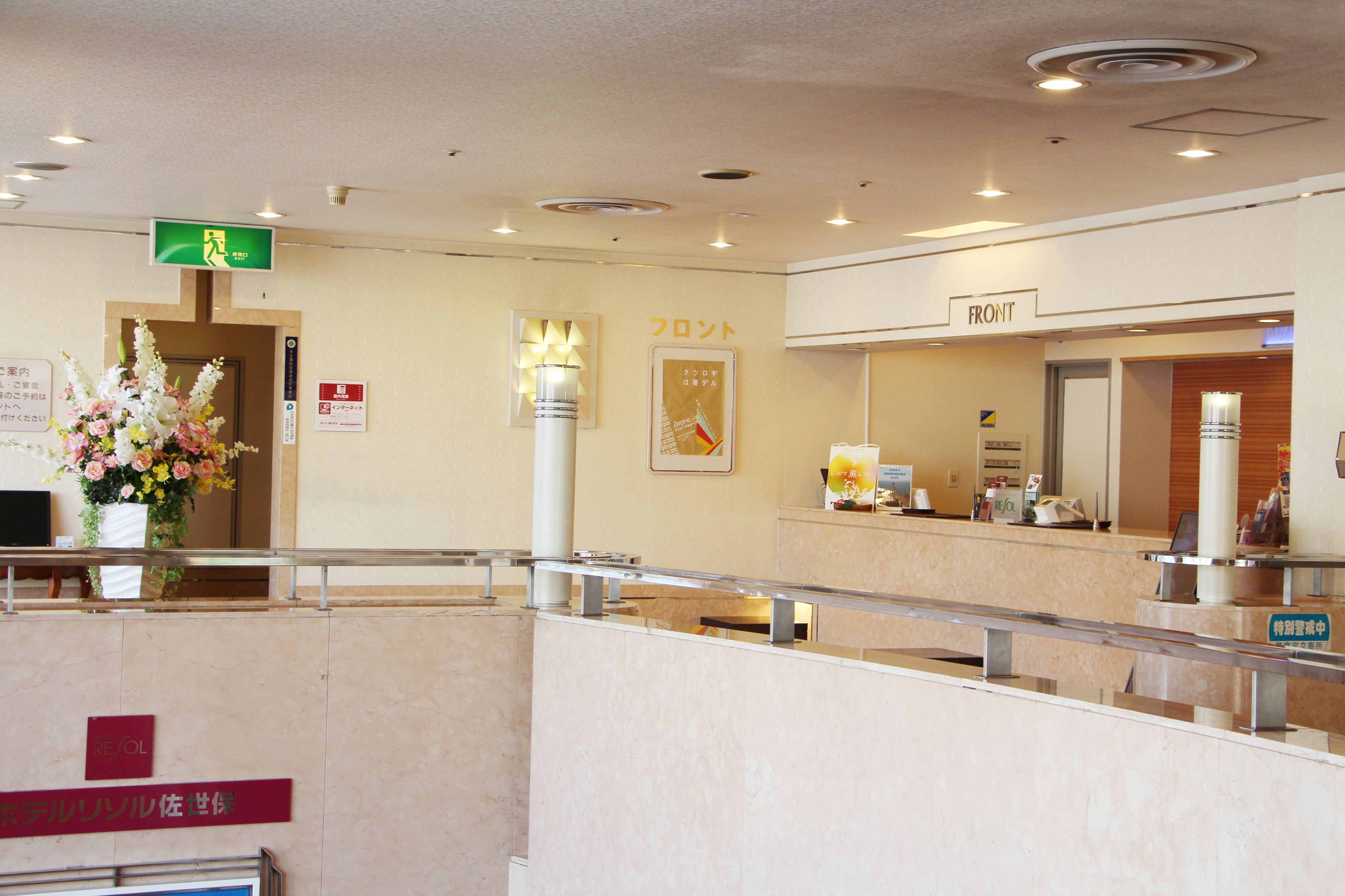 A hotel reception area with a reception desk, a sign indicating the front desk, a flower arrangement, and a sign with Japanese text.