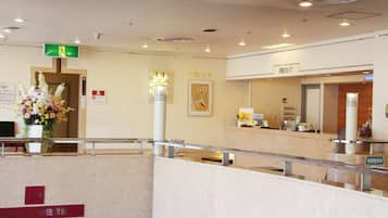 A hotel reception area with a reception desk, a sign indicating the front desk, a flower arrangement, and a sign with Japanese text.