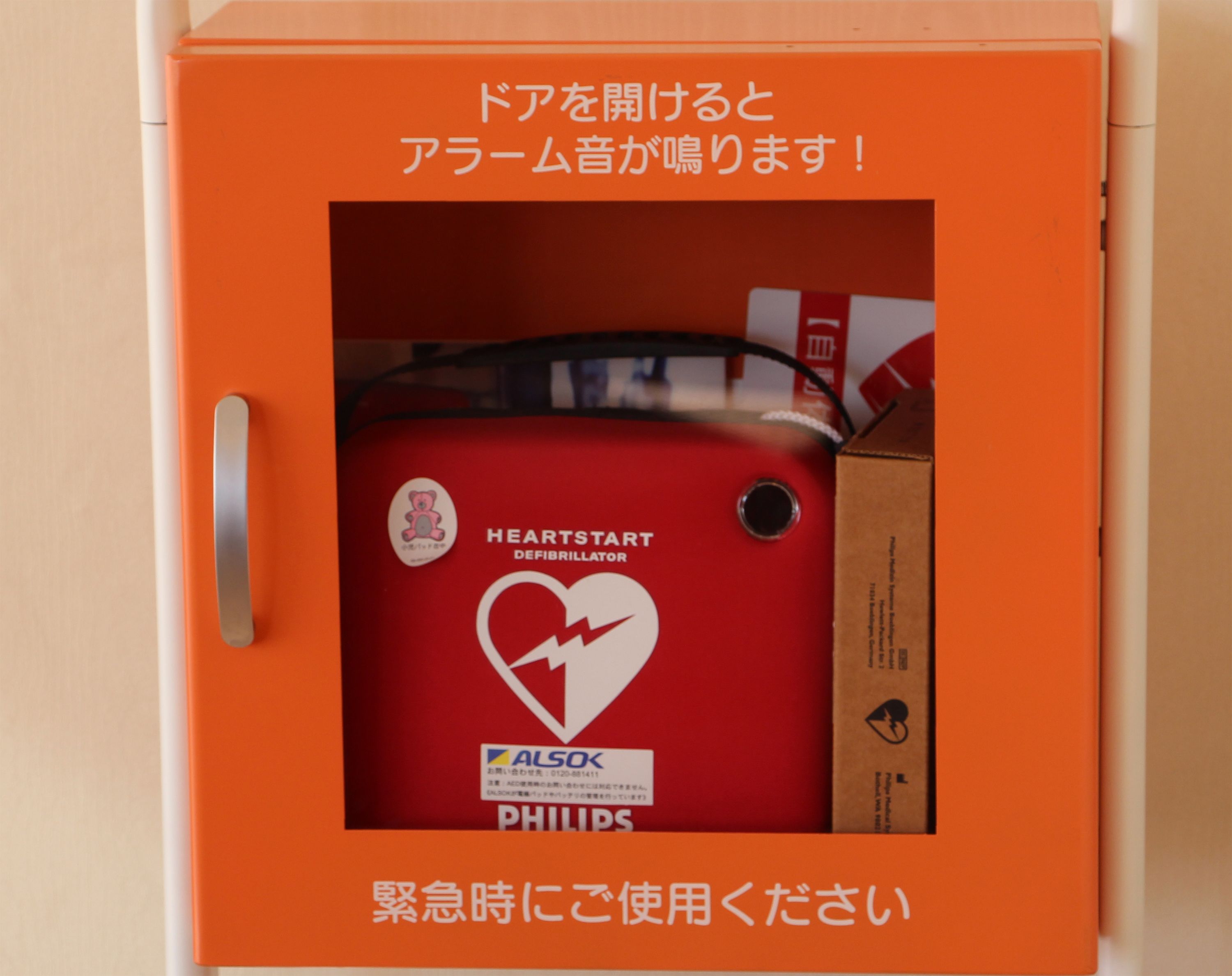 Un desfibrilador rojo en una caja naranja con texto en japonés.