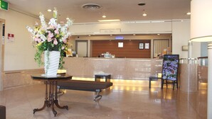 A reception area with a reception desk, a bench, a table with a vase of flowers, and a sign indicating the front desk. - Hotel Resol Sasebo (Sasebo)