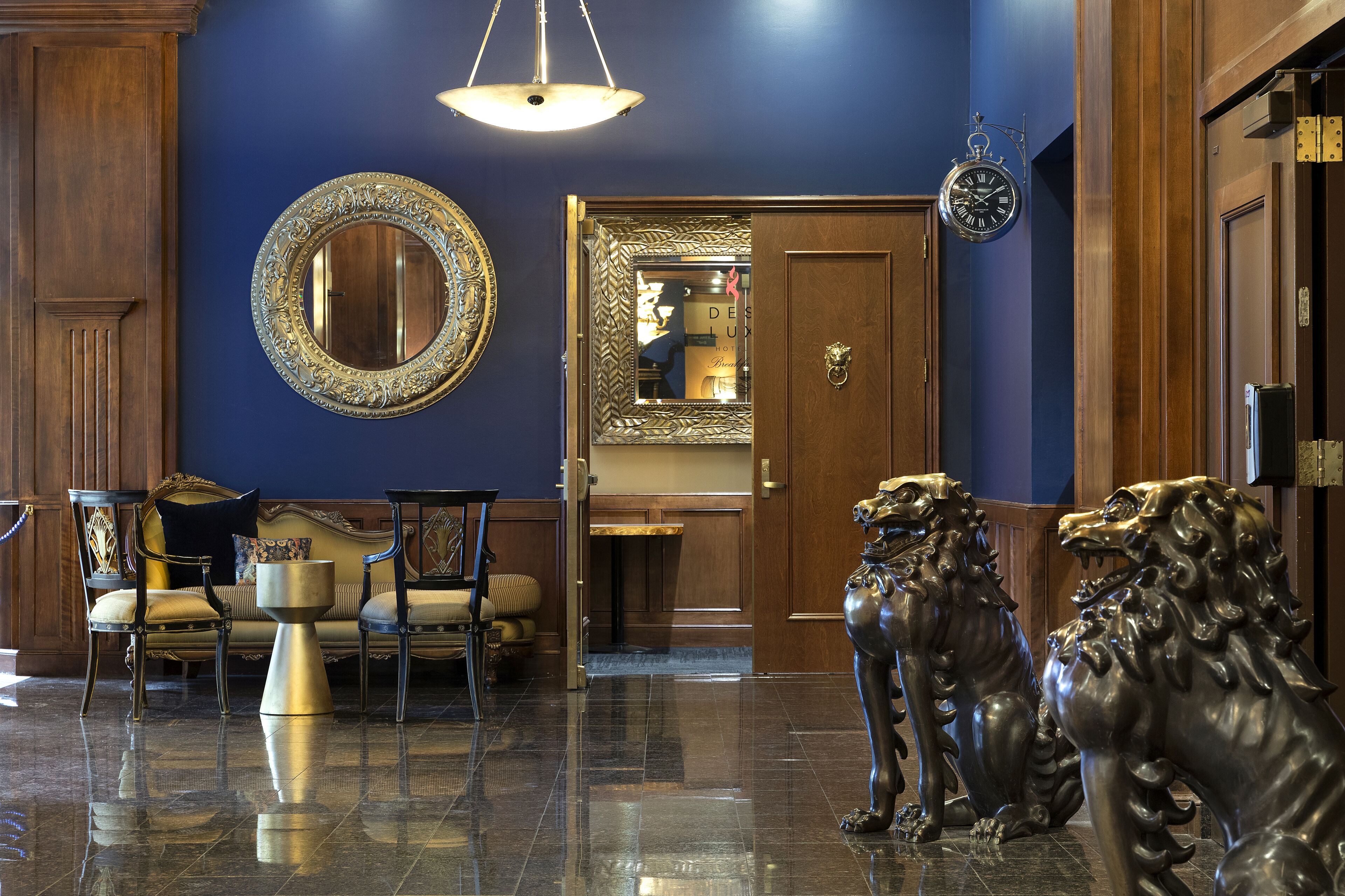 A lobby with a blue wall, a round mirror, a wooden door, and two lion statues.