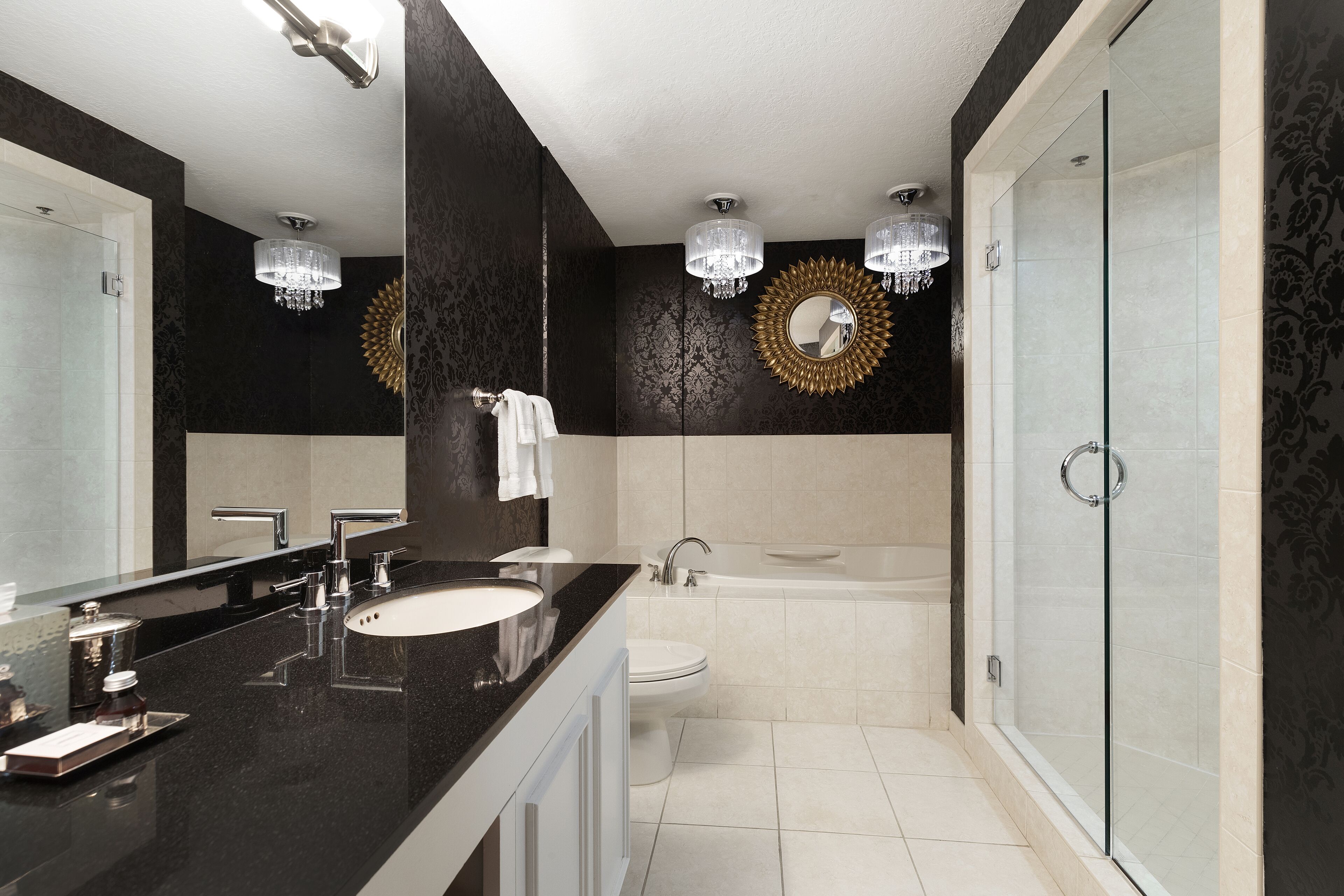 Un baño moderno con encimera negra, lavabo blanco y un espejo grande. Cuenta con una bañera y una ducha con mampara de vidrio.