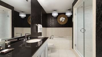 Un baño moderno con encimera negra, lavabo blanco y un espejo grande. Cuenta con una bañera y una ducha con mampara de vidrio.