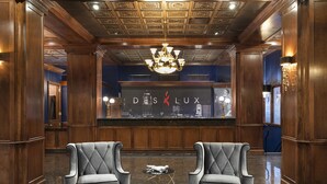 A lobby with two grey upholstered armchairs, a chandelier, and a reception desk displaying the brand name "DS LUX". - Des Lux Hotel (Des Moines)