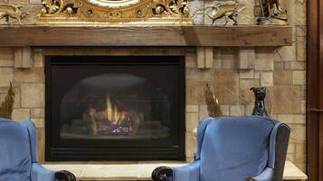 A fireplace with a stone mantle, two blue armchairs, and a decorative mirror above it.