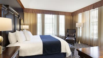 A hotel room with a large bed, a desk, a chair, and a lamp.