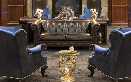 A luxurious living room with a stone fireplace, a large mirror, and two blue armchairs.