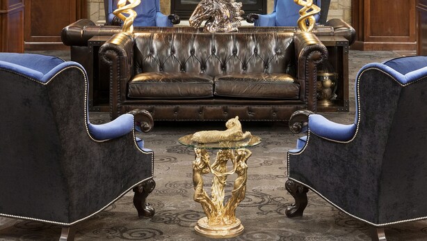 A luxurious living room with a stone fireplace, a large mirror, and two blue armchairs. - Des Lux Hotel (Des Moines)
