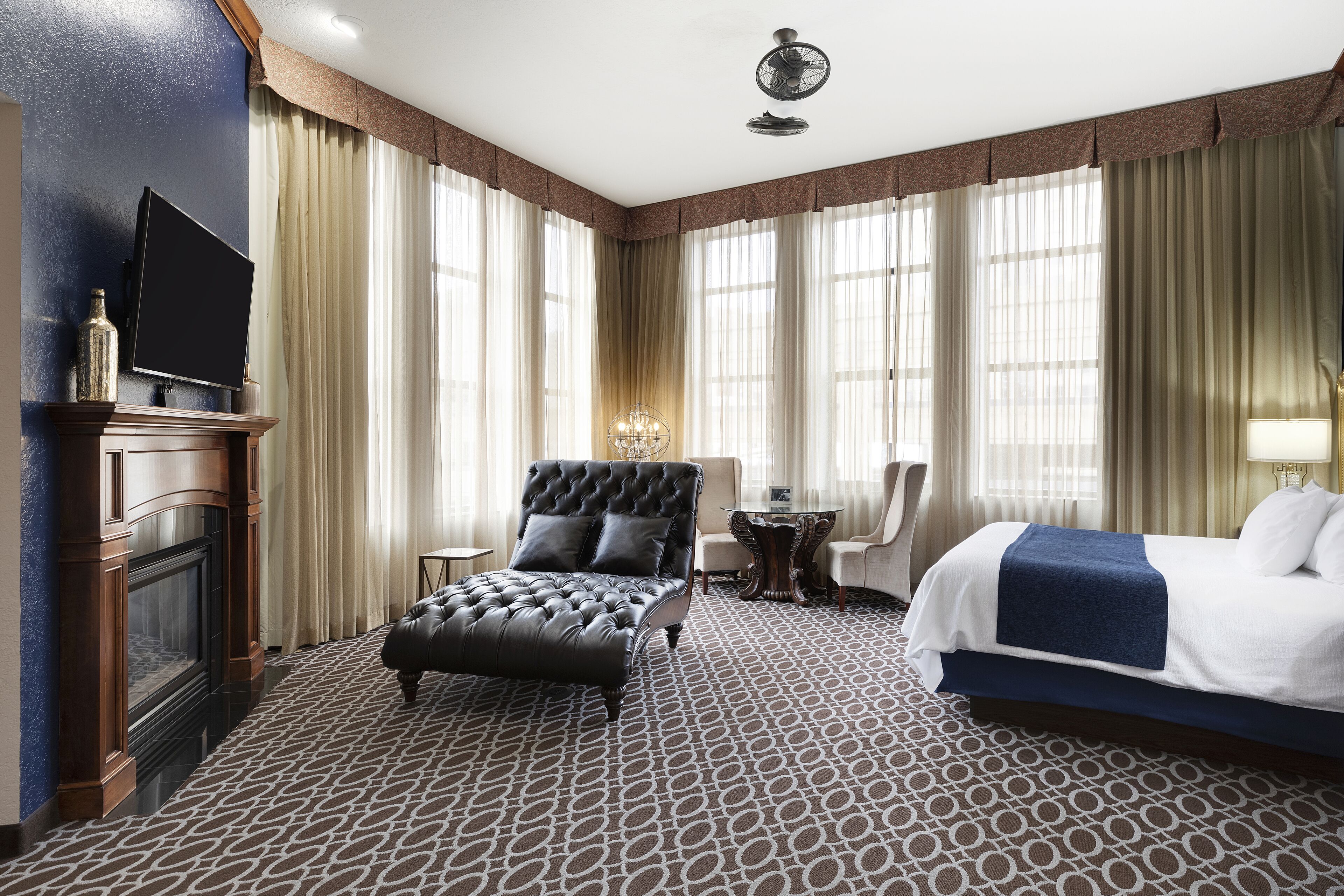 Habitación de hotel con una cama grande, una zona de estar con una silla y una mesa, chimenea y televisor.
