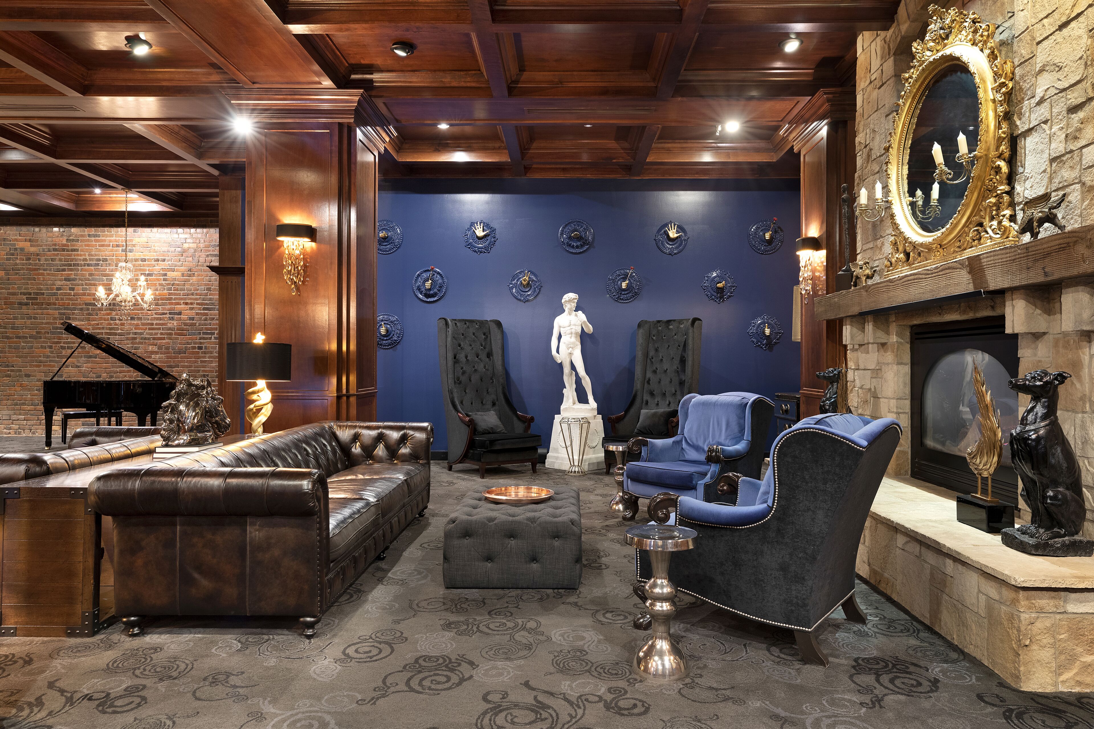 A luxurious living room with a grand piano, leather sofas, a blue armchair, and a fireplace with a decorative mirror.