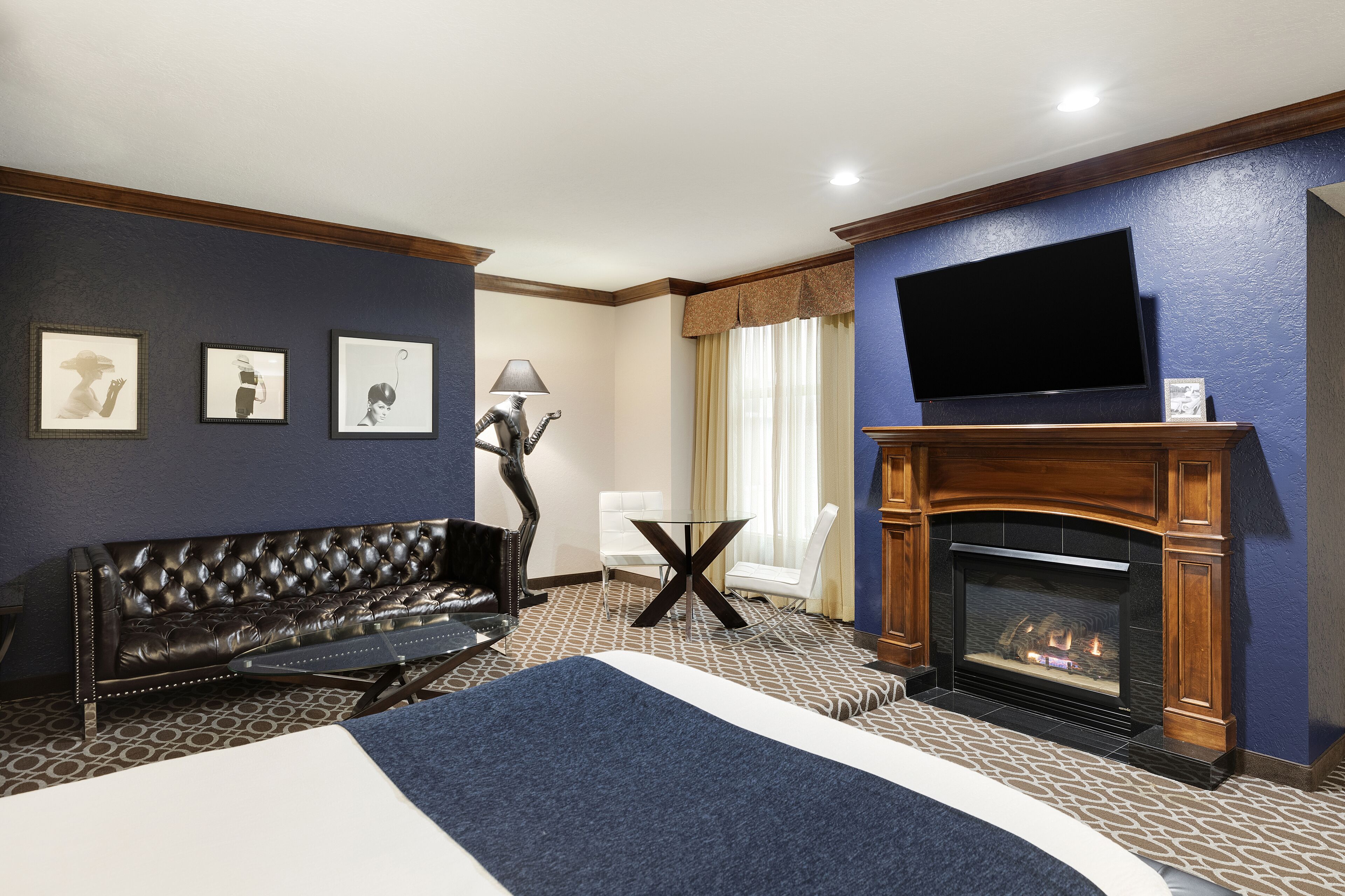 A hotel room with a large bed, a leather sofa, a fireplace, a flat-screen TV, and framed pictures on the wall.