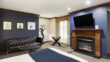 A hotel room with a large bed, a leather sofa, a fireplace, a flat-screen TV, and framed pictures on the wall.