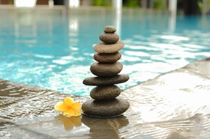 Pilhas de pedras equilibradas à beira da piscina, com uma flor ao lado.