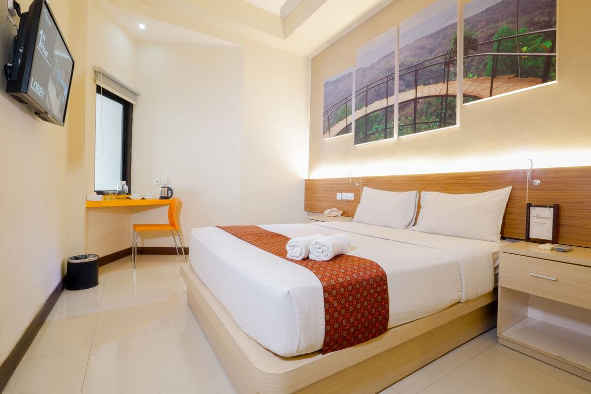 Habitación de hotel con una cama grande, un escritorio, una silla, un televisor y un cuadro en la pared.
