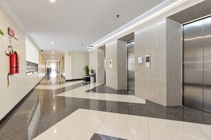 Eine moderne Hotellobby mit einer langen Diele, einem Feuerlöscher, einem Topf mit Pflanze und einem Aufzug.