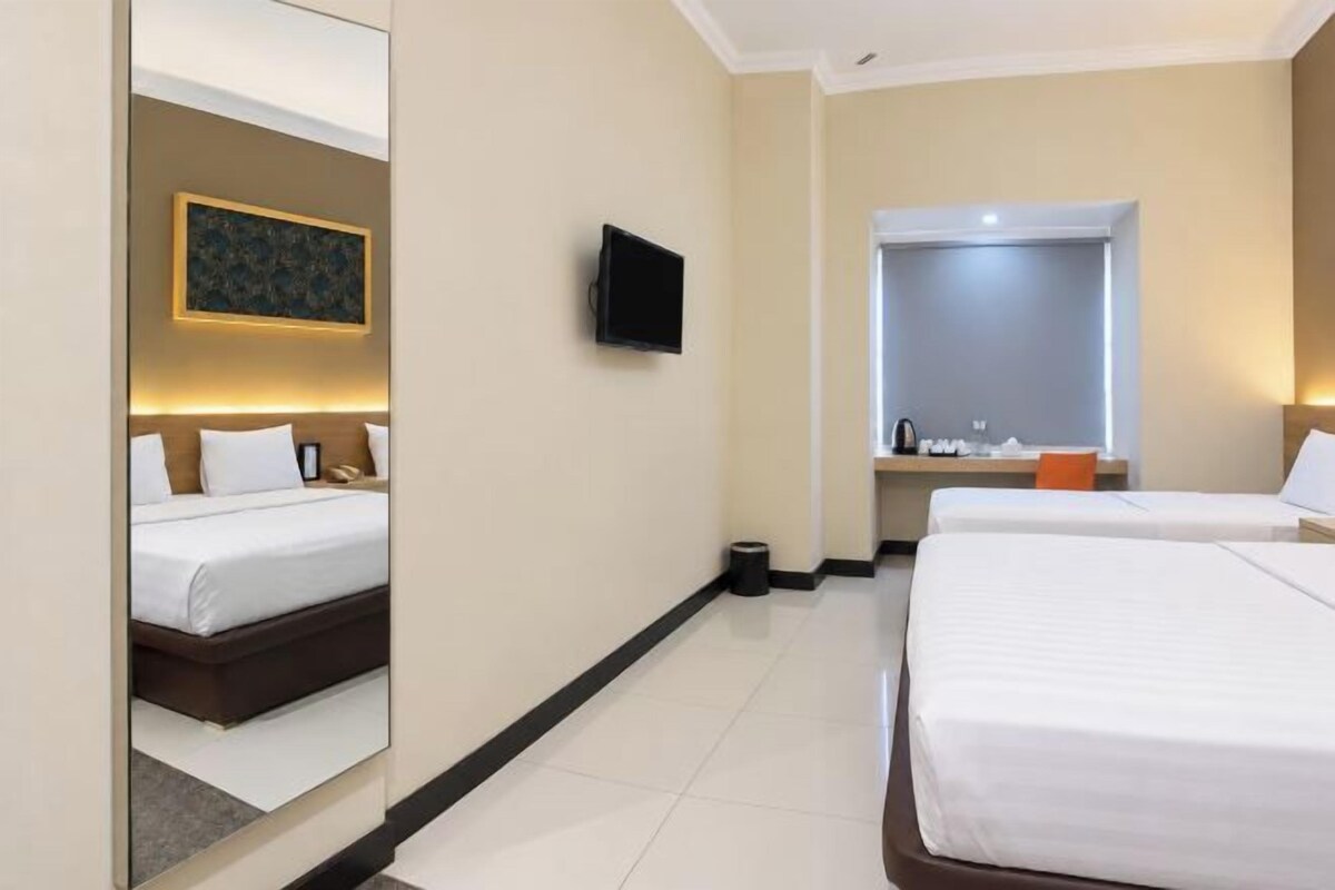A hotel room with a bed, a television, a mirror, and a window.