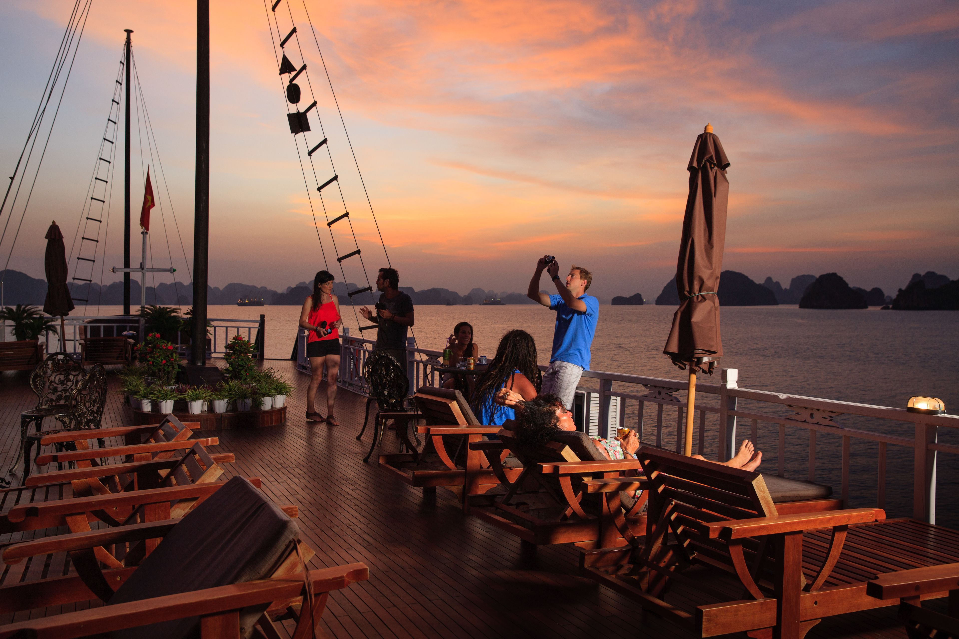 A wooden deck with lounge chairs and tables, overlooking a body of water with distant landforms.