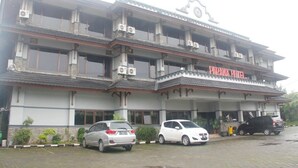 Un edificio de varios pisos con un letrero que dice “PARMA HOTEL”. Hay varios coches estacionados adelante y el edificio tiene múltiples balcones.