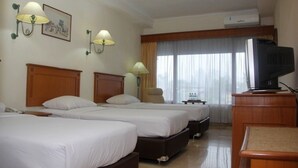 Habitación de hotel con tres camas, un televisor y un escritorio.