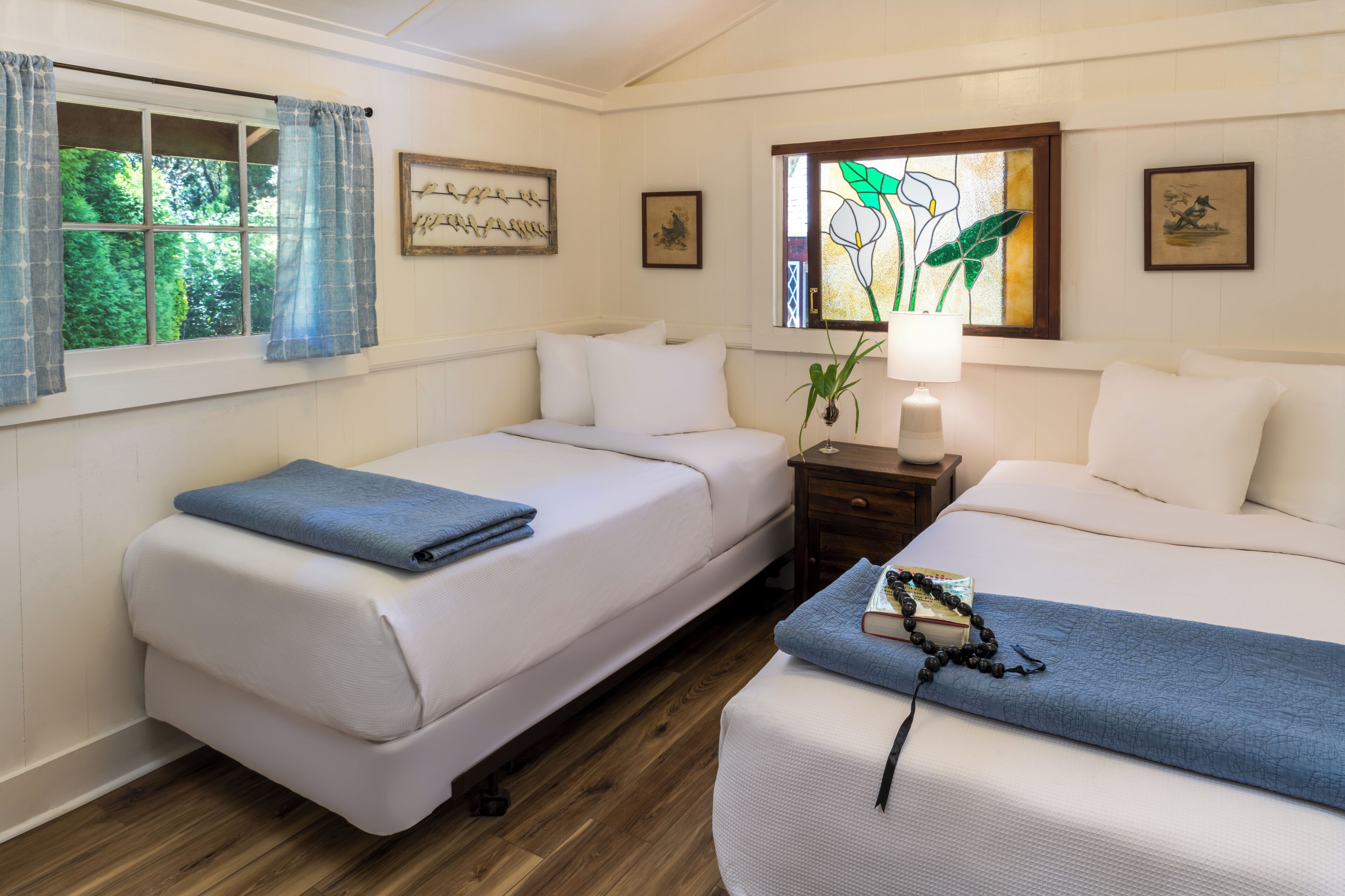 Una habitación con dos camas, una mesita de noche con lámpara y una ventana con cortinas.