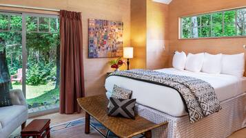 A bedroom with a large bed, a wooden bench, a chair, a window with curtains, and a painting on the wall.