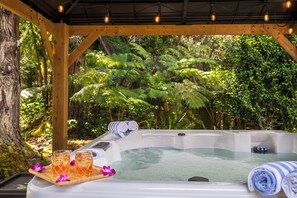 A hot tub with a wooden deck, surrounded by lush greenery and a wooden pergola. - Volcano Village Estates (Volcano)