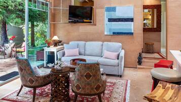 A modern living room with a grey sofa, patterned armchairs, a coffee table, and a TV mounted on the wall.