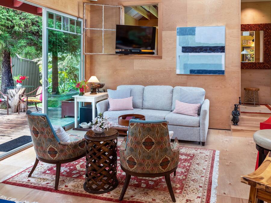 A modern living room with a grey sofa, patterned armchairs, a coffee table, and a TV mounted on the wall.