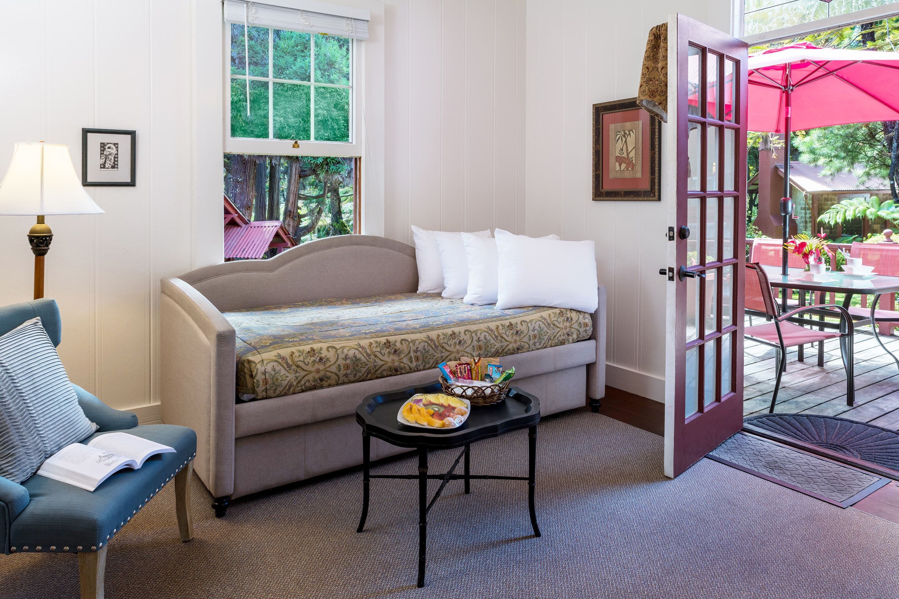 A cozy room with a sofa, a small table with a tray, a chair, and a door leading to an outdoor area with a table and chairs.