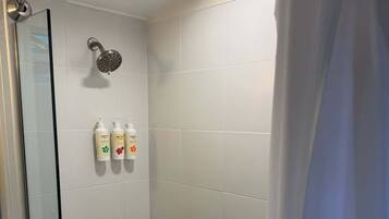 A shower area with a glass door, a handheld showerhead, and three bottles of shampoo and conditioner on the wall.