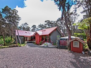 A two-story house with a red roof, surrounded by trees and a gravel driveway. - Volcano Village Estates (Volcano)