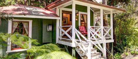 A small, green house with a porch and stairs leading to a door.