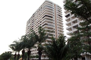 Un edificio alto con varios balcones y una zona arbolada de palmeras alrededor.