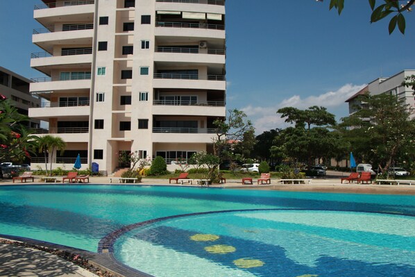 A swimming pool with lounge chairs and a multi-story building in the background. - View Talay 3 Beach Apartments (Pattaya)