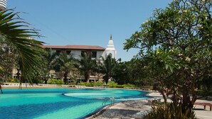 A swimming pool with a clear blue center, surrounded by palm trees and a building with a white spire in the background. - View Talay 3 Beach Apartments (Pattaya)